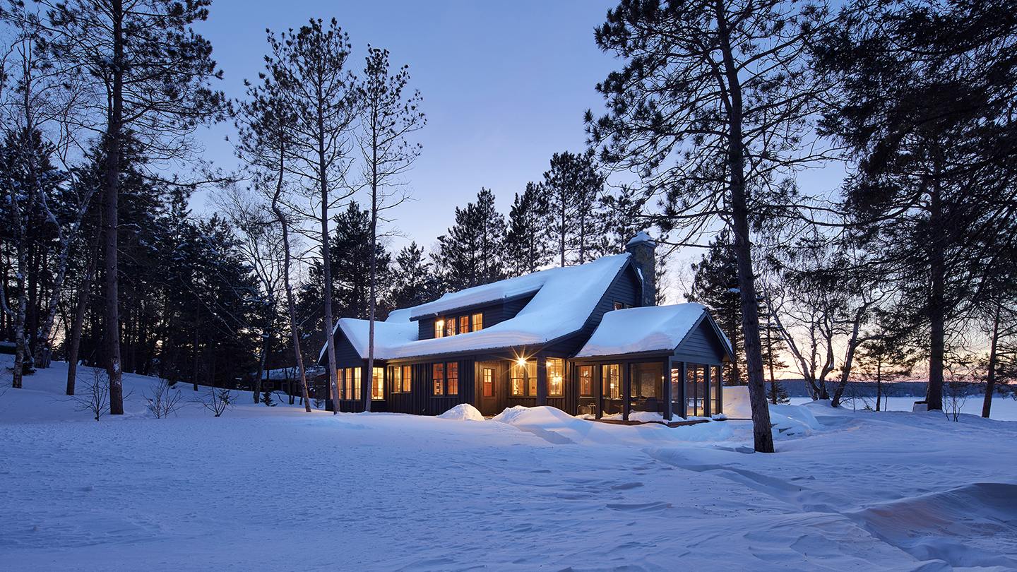 A snow-covered house at dusk, windows glowing